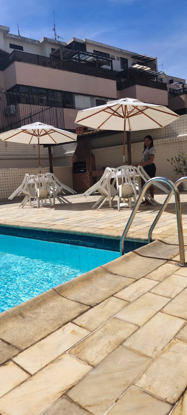 Mesas e cadeiras com ombrelones montados em área de piscina para festa