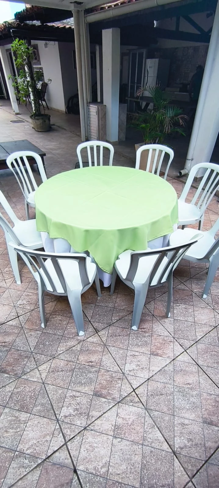 Mesa com toalha verde e cadeiras plásticas montadas para festa em Taquara